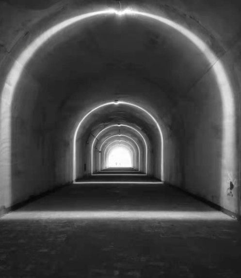 Black-and-white photograph of a tunnel with repeating lit arches